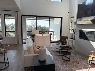 Model Home A cozy living room with a floor-to-ceiling fireplace, large sliding doors, and abundant natural light in Esperanza by Perry Homes (Boerne, TX).