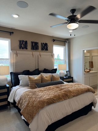 Model Home A cozy bedroom featuring a plush bed with elegant pillows, dual windows, and a ceiling fan, creating a welcoming atmosphere.