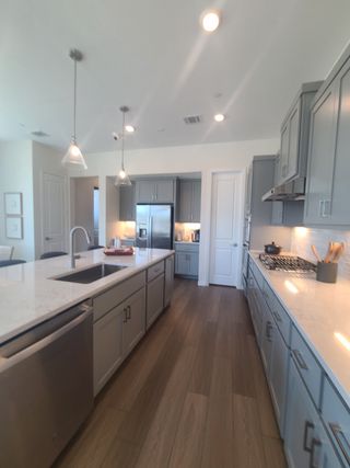A sleek kitchen featuring gray cabinetry, marble countertops, and pendant lighting with stainless steel appliances.