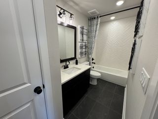 A sleek bathroom featuring dark tile flooring, a black vanity, and herringbone-tiled bathtub wall with modern lighting.