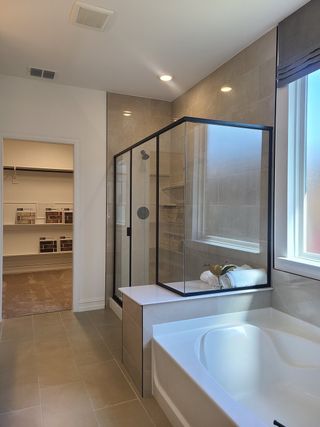 Sleek bathroom with a glass shower, spacious tub, and neutral tiles, leading to a walk-in closet.