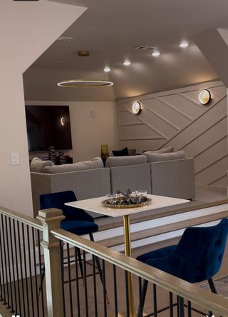 Model Home A modern lounge with geometric wall design, plush gray seating, and chic blue chairs around a white table.