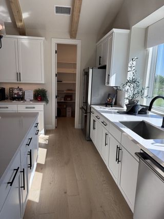 A modern kitchen with sleek white cabinetry, light wood floors, and ample natural light streaming through large windows.