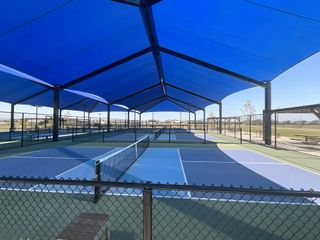 A dedicated sports area featuring multiple pickleball courts under large blue canopies for shade and comfort.
