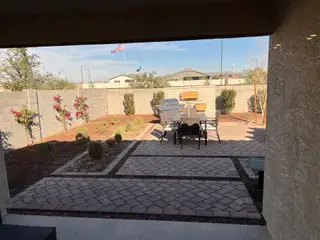 A cozy backyard patio with a dining set and landscaped garden, featuring paver stones and colorful flowers.
