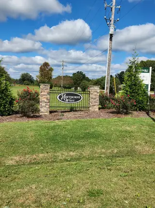 Street view A charming gated entry with a stone accent wall in Hawthorne West by Lennar (Zebulon, NC).