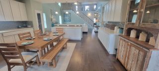 A spacious kitchen with white cabinets, a dining area with a wooden table and benches, and a view of the staircase leading to the upper level.