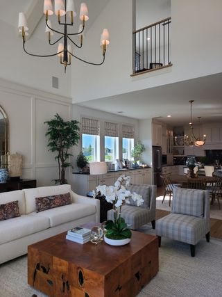 Model Home A spacious living room with elegant chandeliers, plush seating, a wooden coffee table, and open kitchen layout.