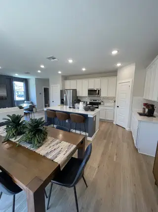 Model Home A modern kitchen with white cabinets, stainless steel appliances, and a cozy dining area with wooden flooring.