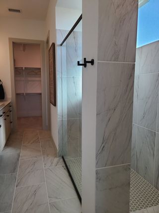 A sleek bathroom with elegant marble tiles, a glass shower, and a well-organized walk-in closet.