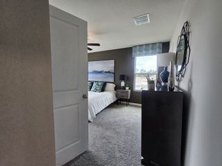 A cozy bedroom with soft carpeting, modern art, and a tall dresser, featuring ample natural light through a large window.