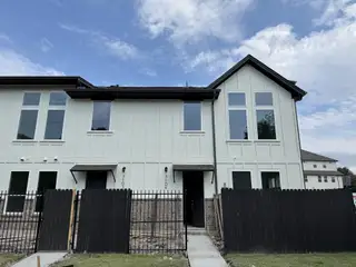 A modern white townhome with large windows and a black fence in Koenig Townhomes by Milestone Community Builders (Austin, TX).