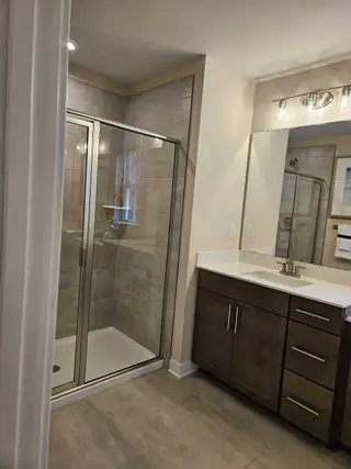 A contemporary bathroom featuring a sleek glass shower, dark wood vanity, and elegant lighting fixtures.