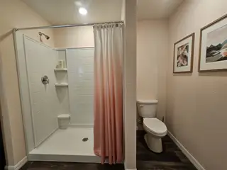 A cozy bathroom featuring a tiled shower, pink curtain, and stylish framed artwork.