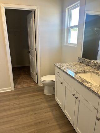 Model Home A bright bathroom with a granite countertop, white cabinetry, and wood flooring, featuring an adjacent walk-in closet.