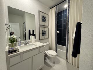 A sleek bathroom features a marble countertop, elegant framed art, and a chic, patterned shower curtain.