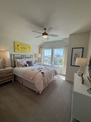 A cozy bedroom with soft décor, a ceiling fan, and large windows offering natural light and a serene atmosphere.
