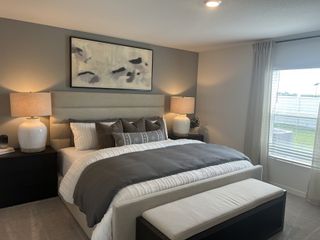 A cozy bedroom featuring a plush bed with neutral bedding, elegant lamps, abstract art, and natural light from a large window.