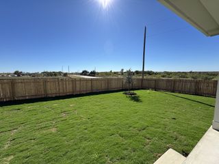 A lush green backyard under a clear blue sky, enclosed by a wooden fence in Calumet by Brightland Homes (Jarrell, TX).