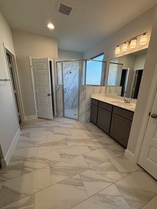 A modern bathroom with a sleek glass shower, marble-tiled floor, double vanity, and elegant lighting.