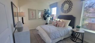 A serene bedroom in a Marbella home, featuring a plush bed with decorative pillows, a sunburst mirror, a patterned rug, and ample natural light (San Antonio, TX).