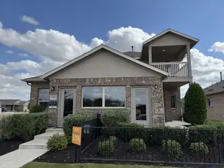 Street view A charming brick home with a second-floor balcony in the Village at Manor Commons by Pacesetter Homes (Manor, TX).