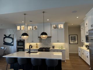 Model Home Elegant kitchen featuring white cabinets, modern pendant lighting, and a spacious island with sleek barstools.
