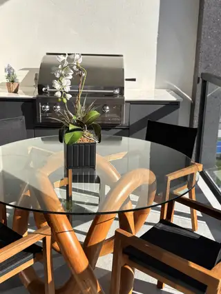 A modern patio with a unique glass table, wooden chairs, and a sleek grill, perfect for outdoor dining and entertainment.