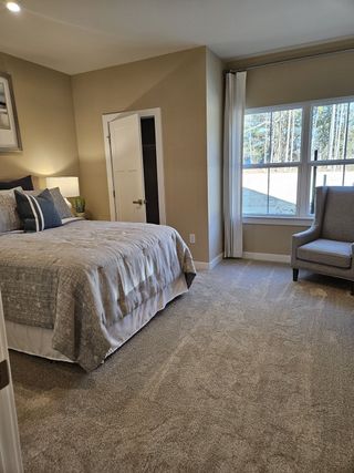 Cozy bedroom with neutral tones, plush carpet, elegant bedding, and a large window for natural light.