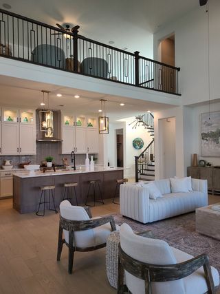 Model Home A spacious living area with an open floor plan, featuring a modern kitchen, elegant furnishings, and a stylish staircase.