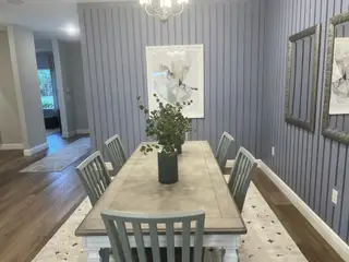 A cozy dining room featuring a wood table, elegant gray chairs, and blue paneled walls with modern artwork.