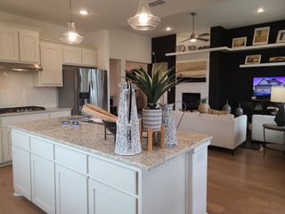 Model Home A modern kitchen with a granite island, sleek cabinetry, pendant lighting, and open living space featuring a cozy lounge area.