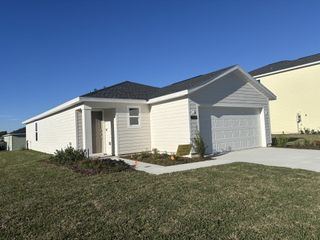 A bright, sunny day highlights a white single-story home in Millwood Estates (Ocala, FL) by Lennar, with a two-car garage and a newly planted tree.