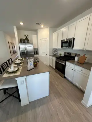 Model Home A modern kitchen with white cabinets, stainless steel appliances, and a sleek island with seating for two.