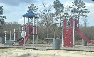 A colorful playground with slides, climbing structures, and benches, situated in a park with tall trees in the background in Dacula, GA.