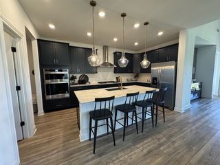 A modern kitchen with dark cabinets, a large island, pendant lighting, and stainless steel appliances.