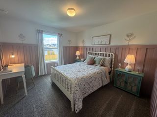 A cozy bedroom with a patterned bed, elegant wall panels, a teal nightstand, and a small workspace by the window.