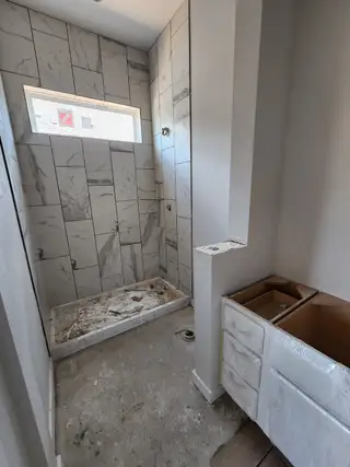 Model Home A bathroom under construction featuring marble-tiled walls, a window for natural light, and an unfinished vanity.