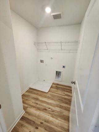 A bright laundry room with wood-look flooring, wire shelving, and hookups, ready for a washer and dryer installation.