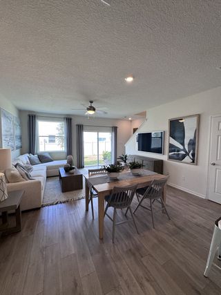 A cozy living and dining area featuring wood floors, a neutral sofa, a wooden table, and modern decor with natural light.