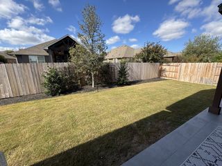 A spacious backyard with a lush lawn and wooden privacy fence in Hawkes Landing by Brightland Homes (Leander, TX).