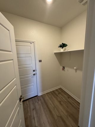 A cozy utility room with wood flooring, white walls, and shelving for storage.