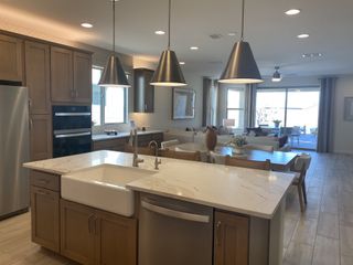 Model Home A bright, open kitchen with a farmhouse sink, quartz counters, and pendant lighting flows into a living area with natural light and patio access.