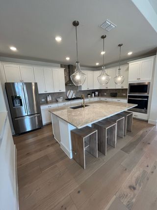 Model Home A modern kitchen with elegant pendant lights, stainless steel appliances, a spacious island, and sleek white cabinetry.