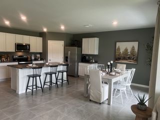 A bright, open-concept kitchen and dining area with white cabinets, stainless steel appliances, and a gray accent wall.