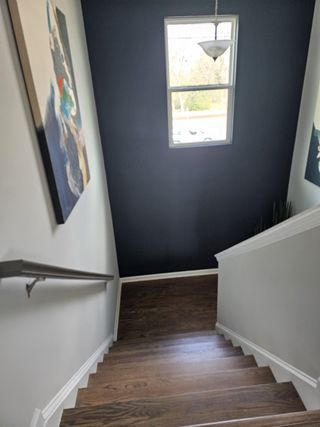 A staircase featuring wood-look treads and white risers leads down to a lower level, highlighted by a dark blue accent wall with a window and a modern pendant light.