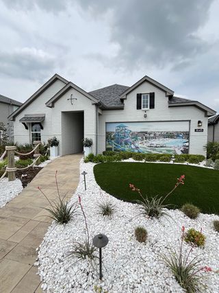 Street view A charming white brick home with shutters and a landscaped yard in Venetian by Megatel Homes (Celina, TX).