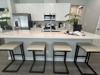 A modern kitchen with sleek white cabinetry, stainless steel appliances, and a spacious island with four contemporary bar stools.