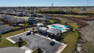 A resort-style pool with shaded lounge areas and a clubhouse in The Villages at Schwertner Ranch by D.R. Horton (Jarrell, TX).