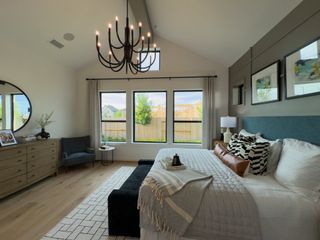 A cozy bedroom featuring elegant lighting, a large bed, stylish artwork, and a beautiful view through large double windows.